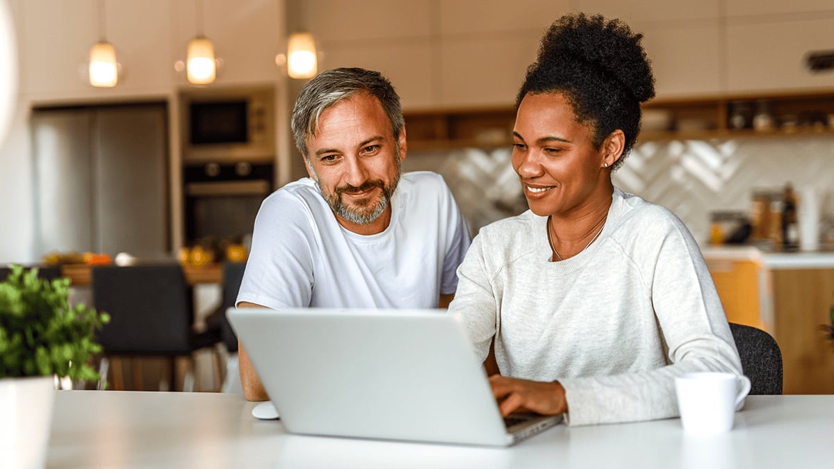 Couple planning finances on a laptop in their kitchen.