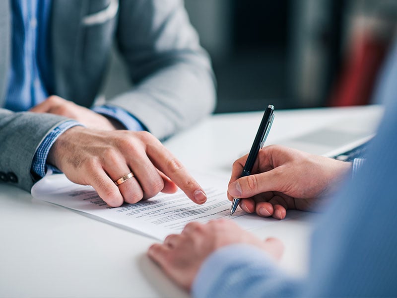 A businessman's hand pointing to show another person where to sign